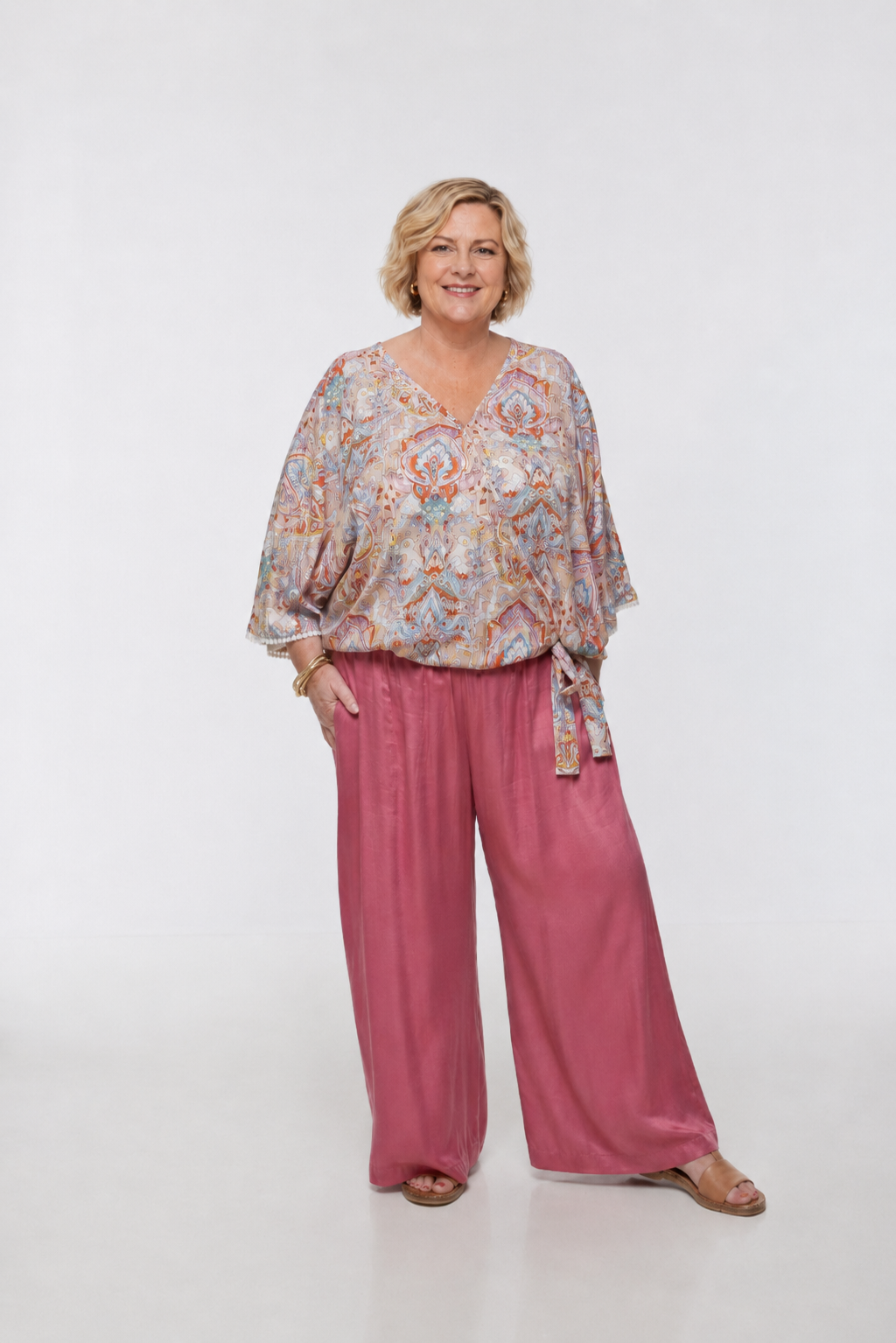 Woman wearing the Messina Top - Palazzo Print. A flowing printed rayon top with a wrap-over neckline, kimono sleeves, crochet trim, elastic waist with adjustable tie