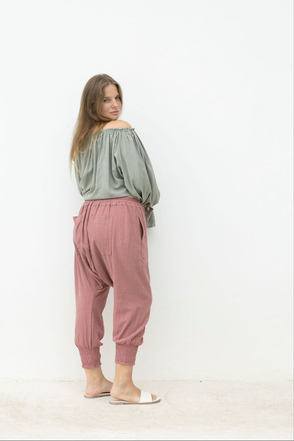 Woman wearing a green off-shoulder top and pink pants against a white background