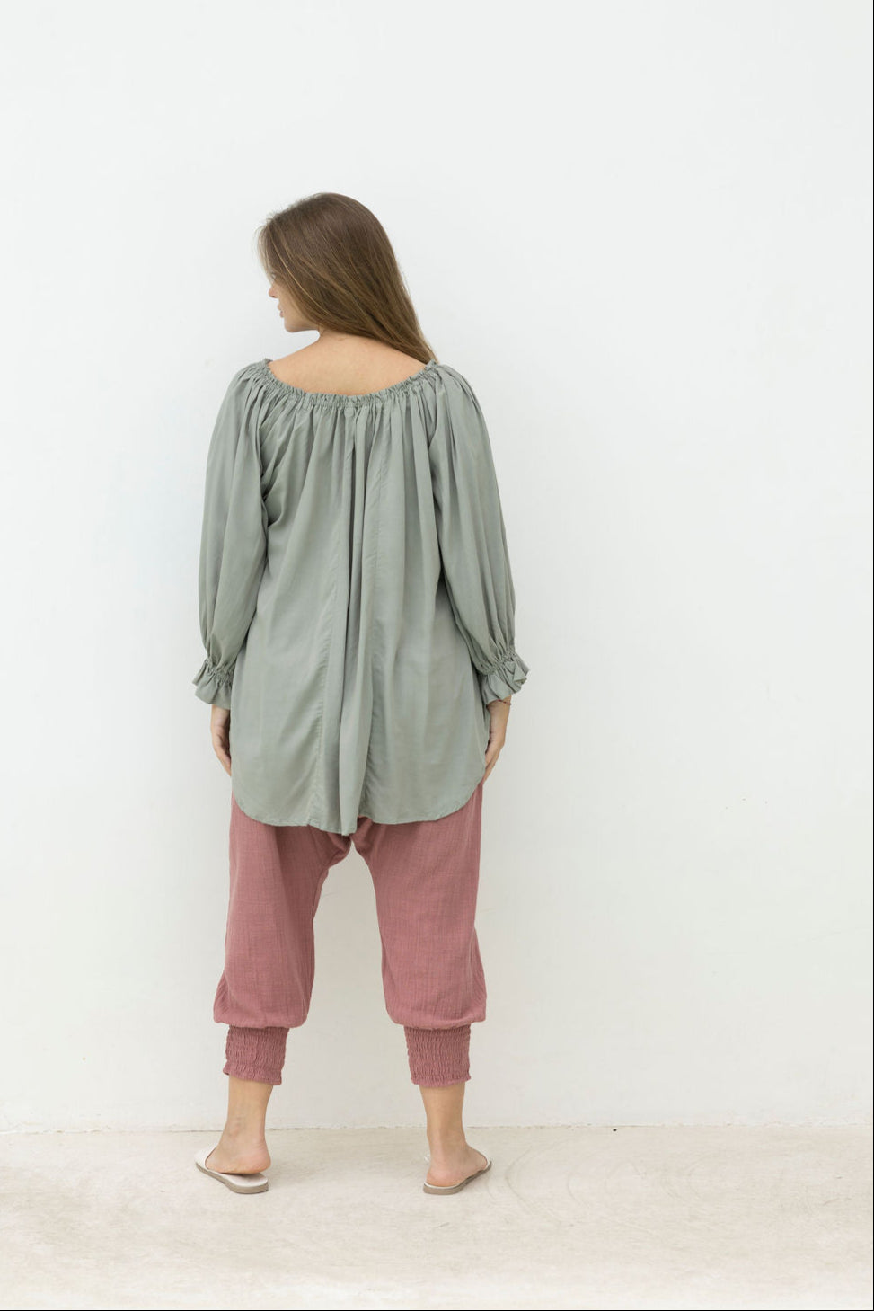 Woman wearing a green top and pink pants against a white background