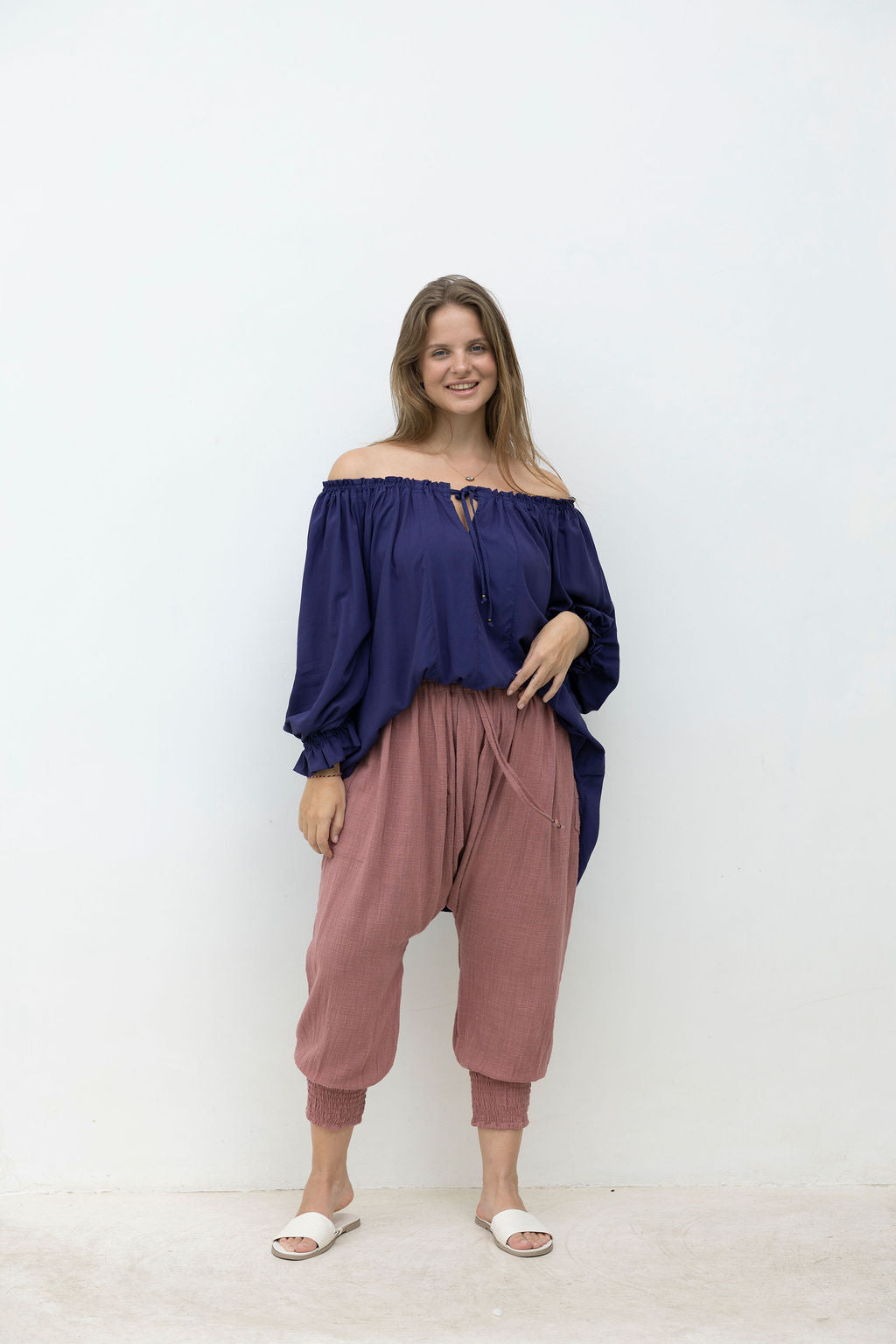 Woman wearing a blue off-shoulder top and pink pants against a white background