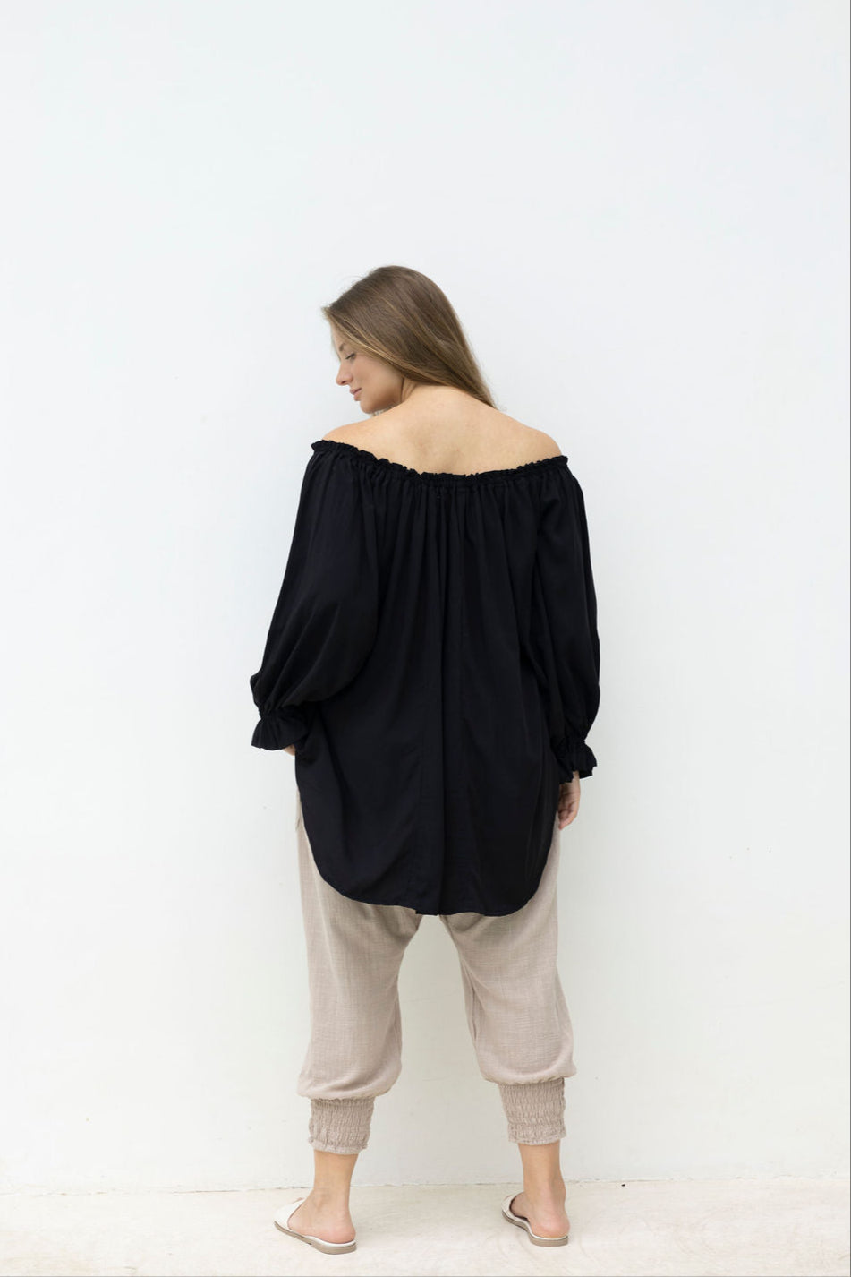 Person wearing a black off-shoulder top and beige pants against a white background