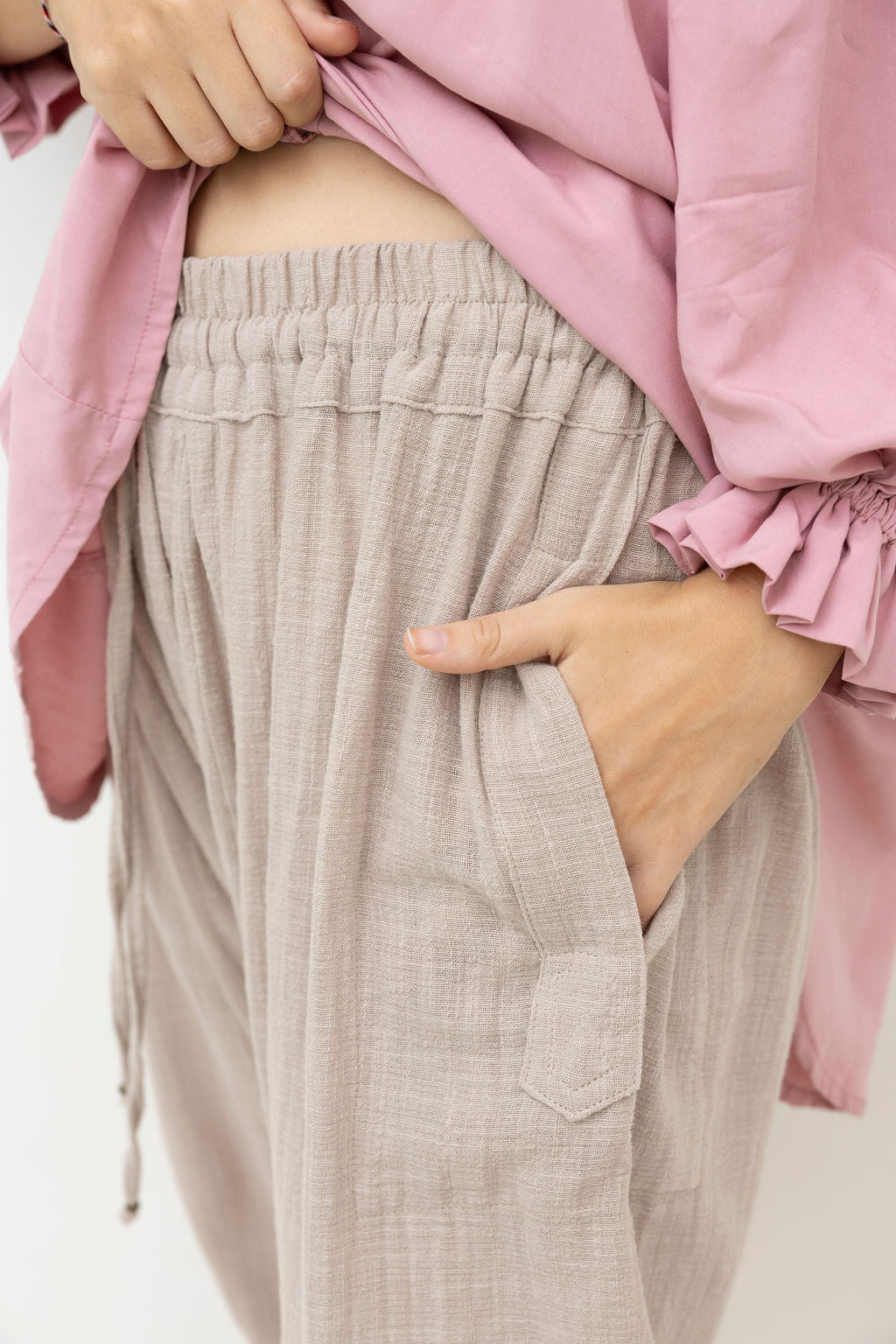 Person wearing a pink shirt and beige pants with a white background