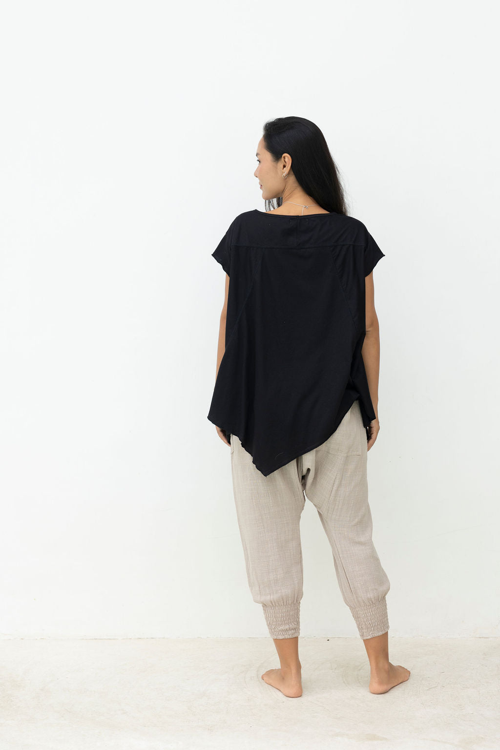 Woman wearing a black top and light gray pants against a white background