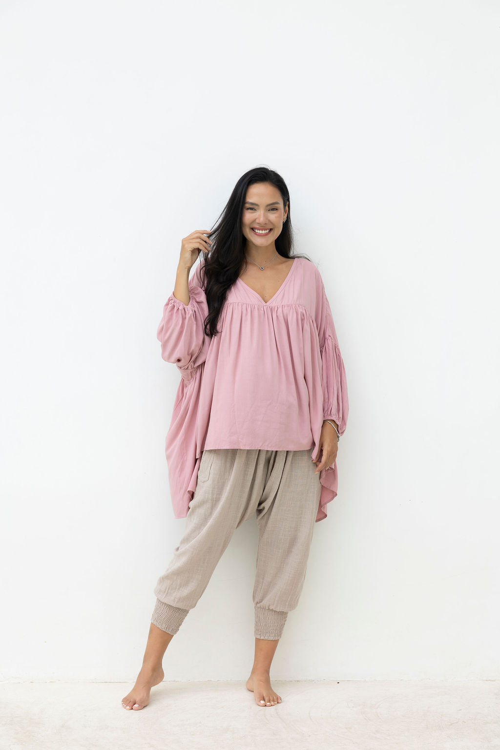 Woman wearing a pink blouse and beige pants on a white background
