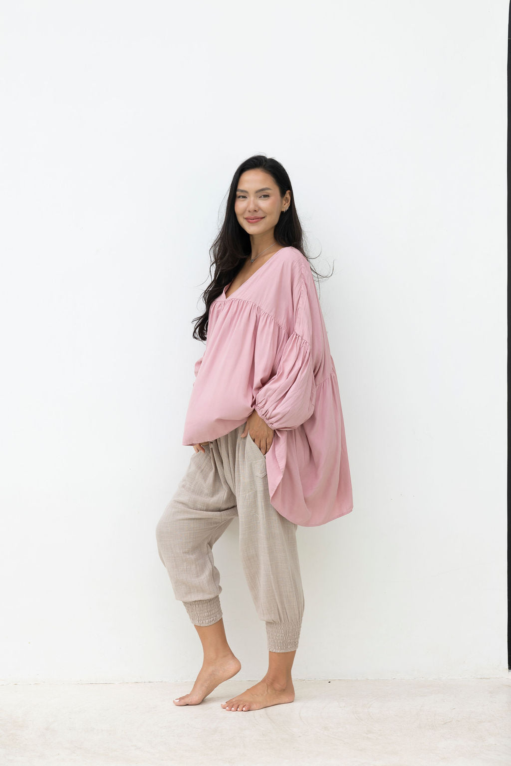 Woman wearing a pink oversized top and beige pants against a white background