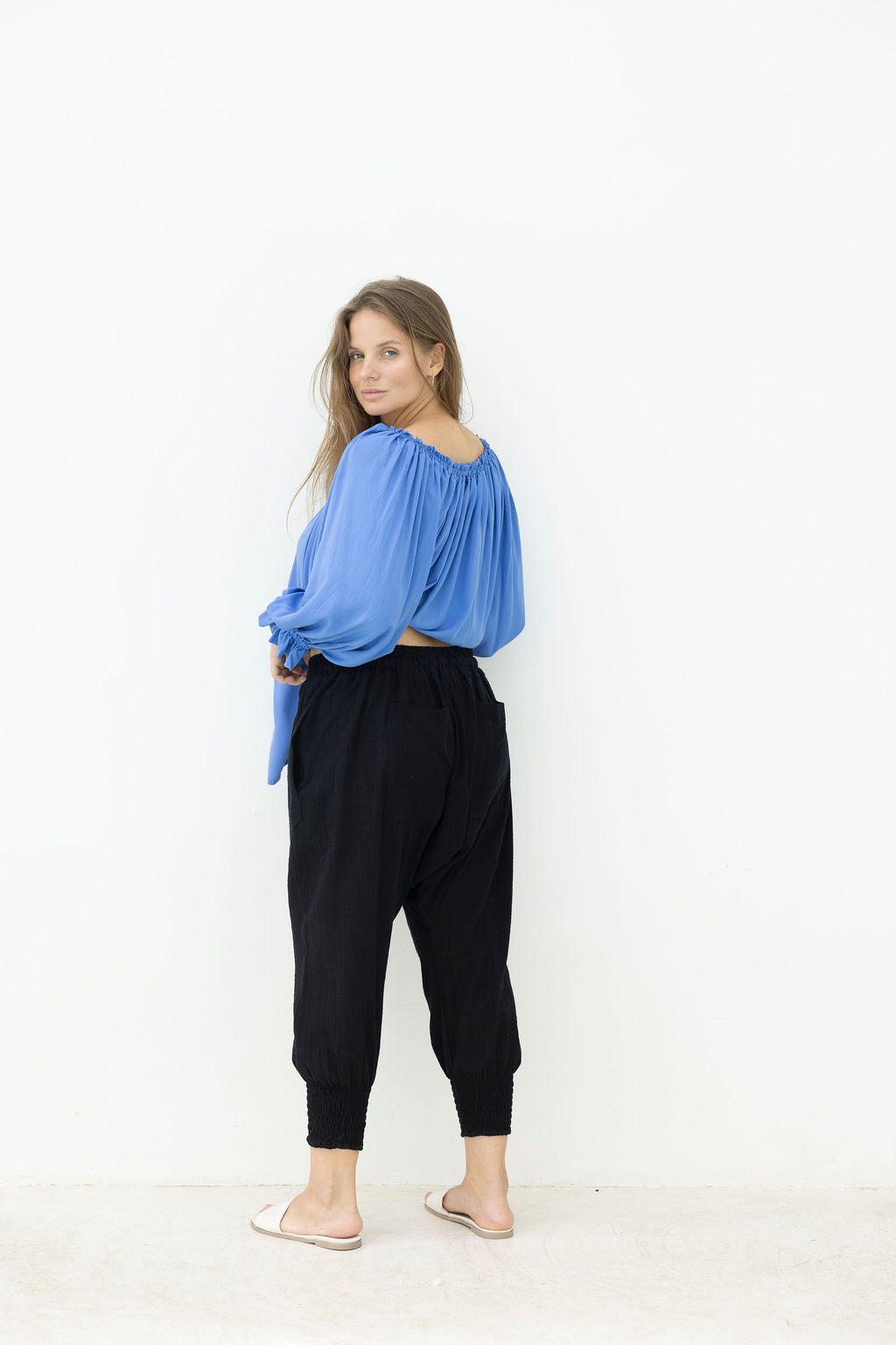 Woman wearing a blue top and black pants against a white background