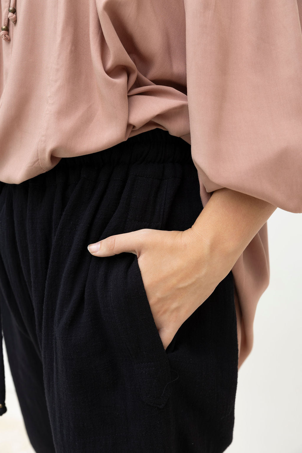 Person wearing a pink top and black pants with one hand in a pocket against a white background