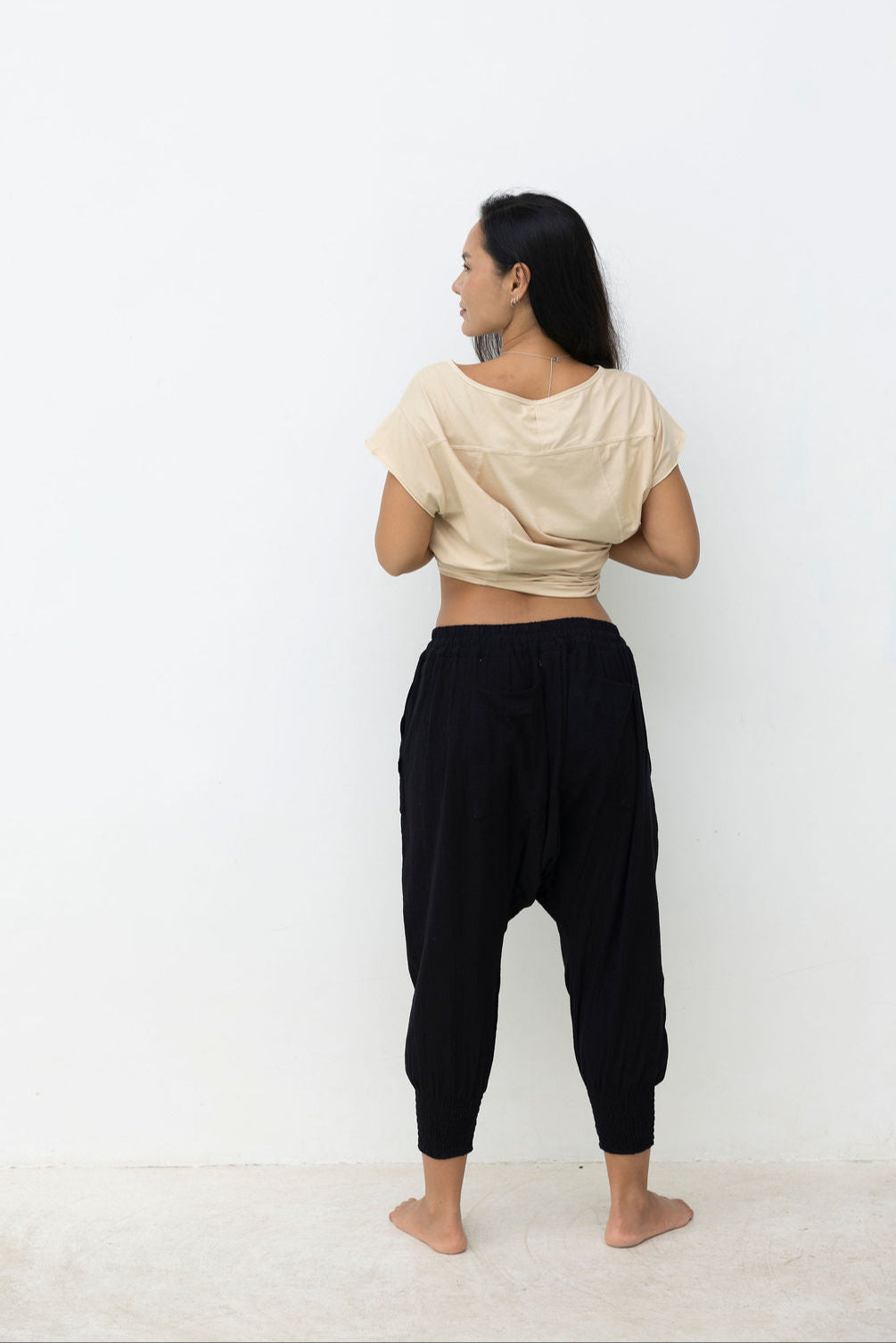 Person wearing a beige top and black pants against a white background