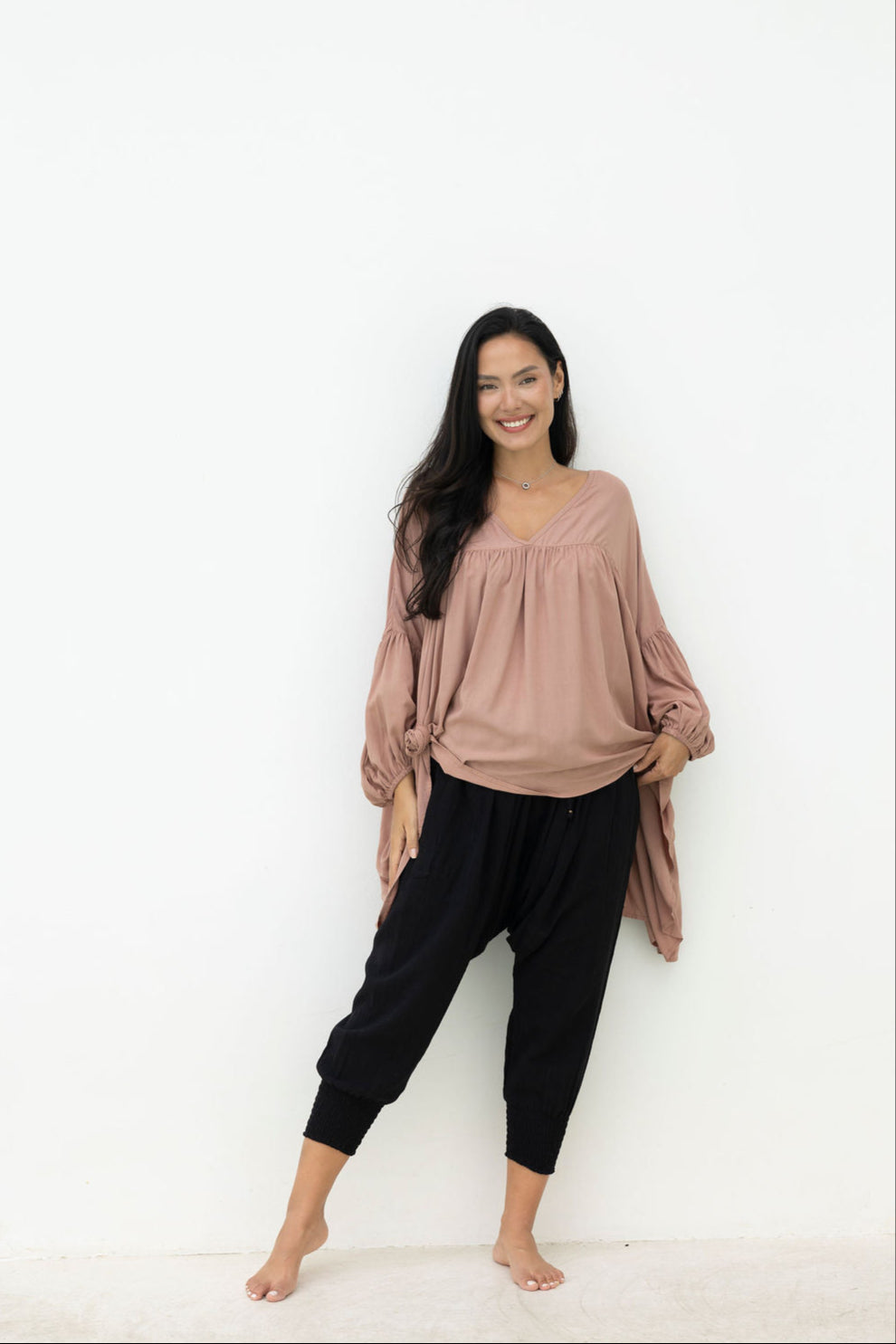 Woman wearing a loose-fitting pink top and black pants against a white background