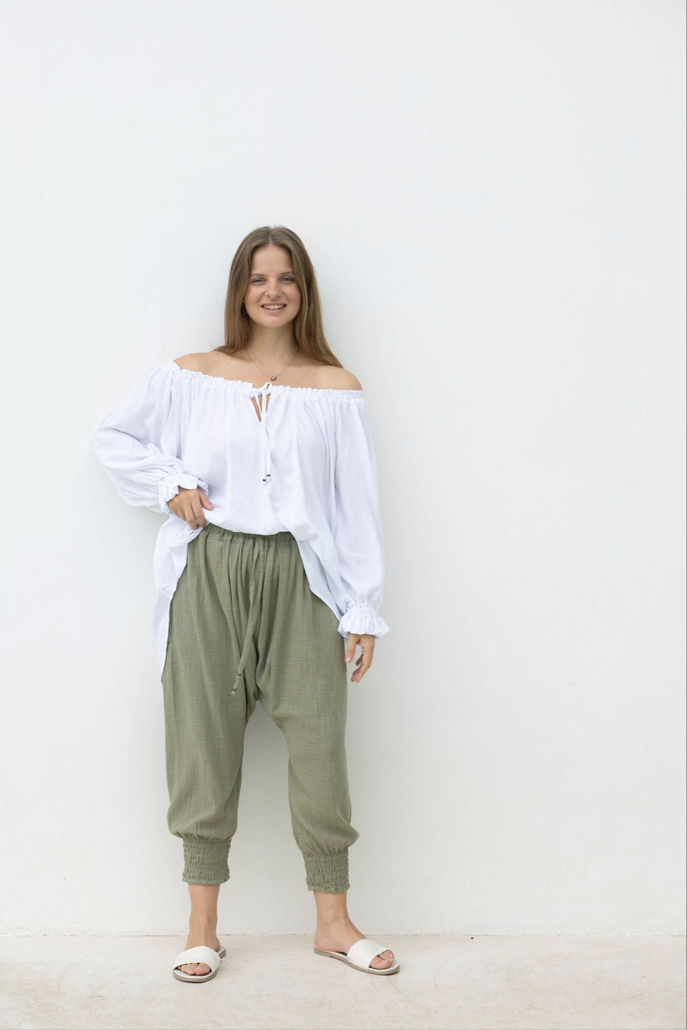 Woman wearing a white off-shoulder top and green pants against a white background