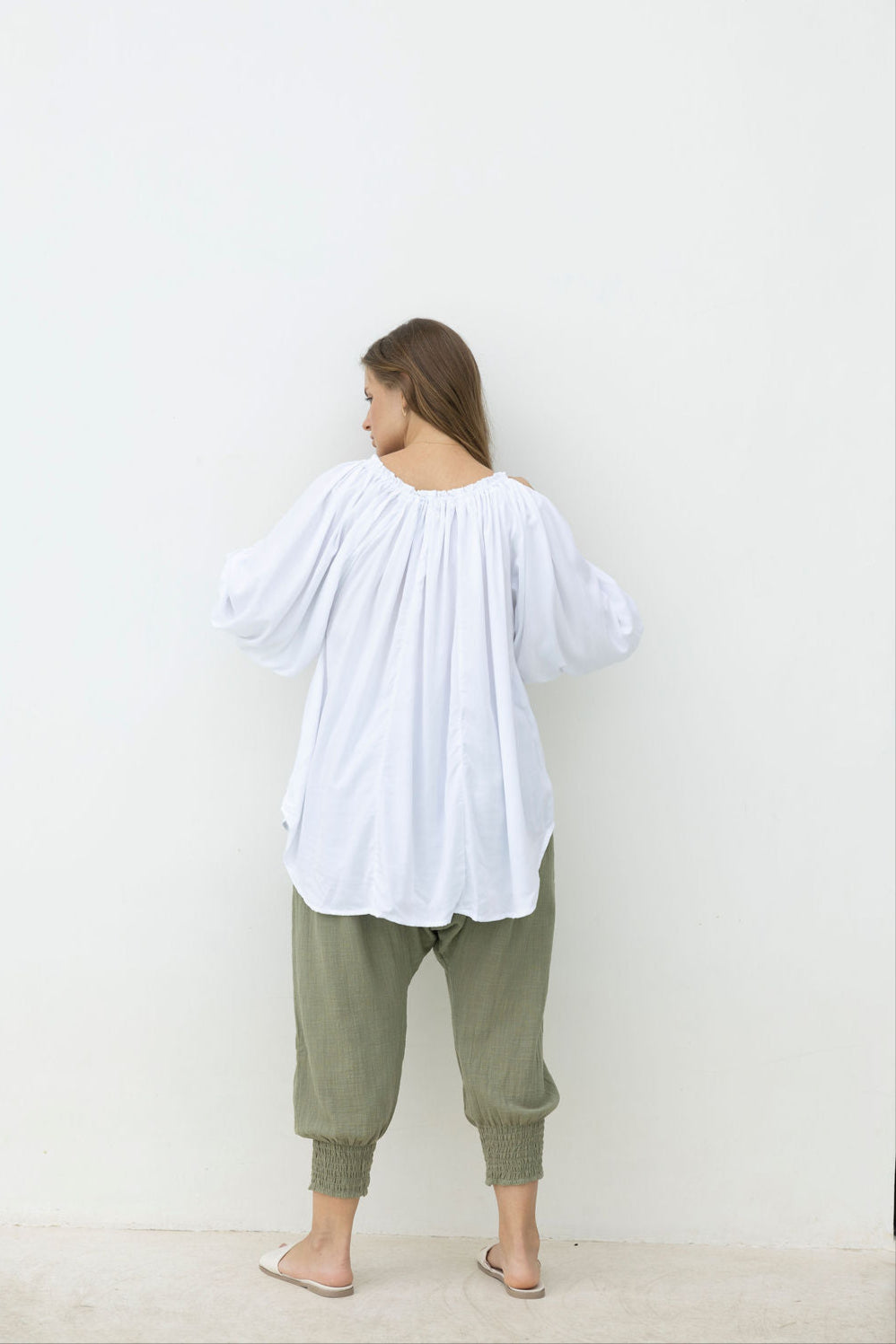 Person wearing a white blouse and green pants against a plain background