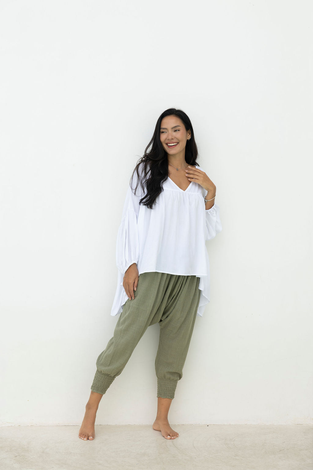 Woman wearing a white blouse and green pants against a white background