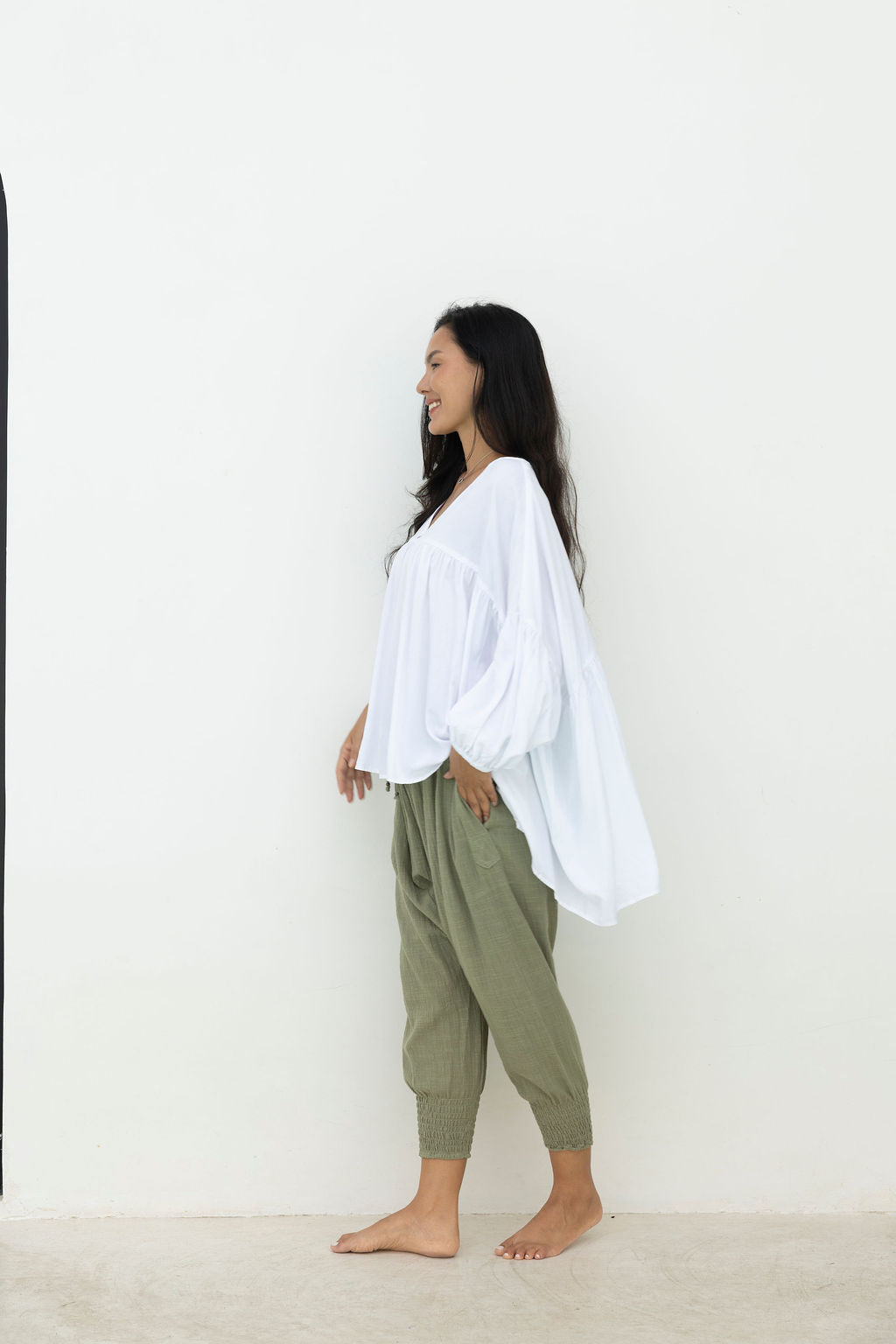 Woman wearing a white top and green pants against a plain background