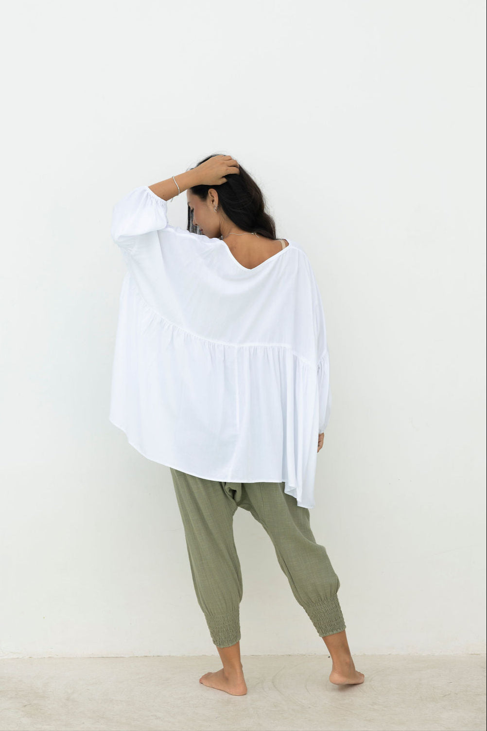 Person wearing a white oversized top and green pants against a plain background