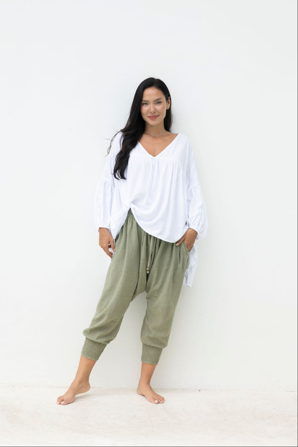 Woman wearing a white top and green pants against a white background
