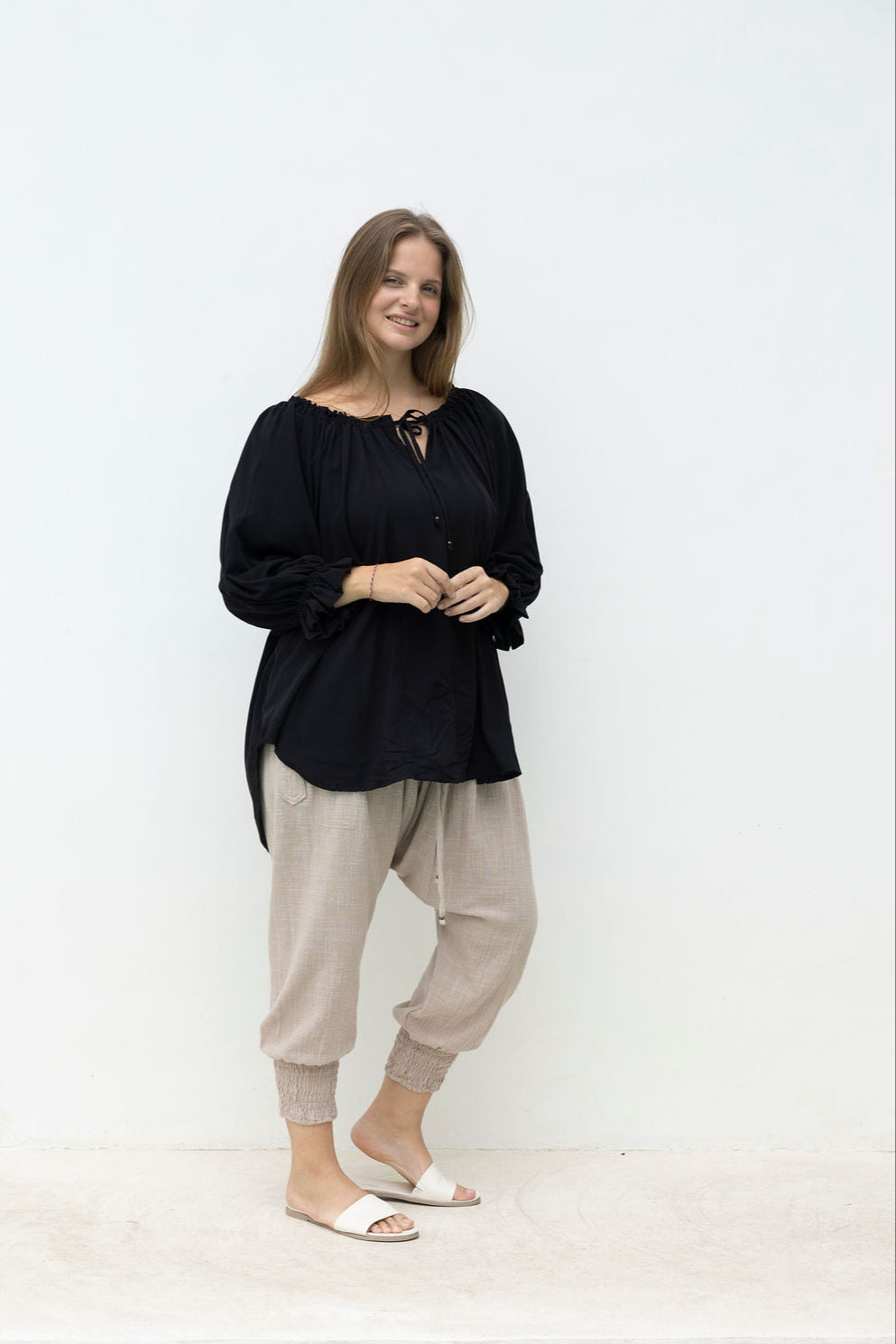 Woman wearing a black top and beige pants standing against a white background