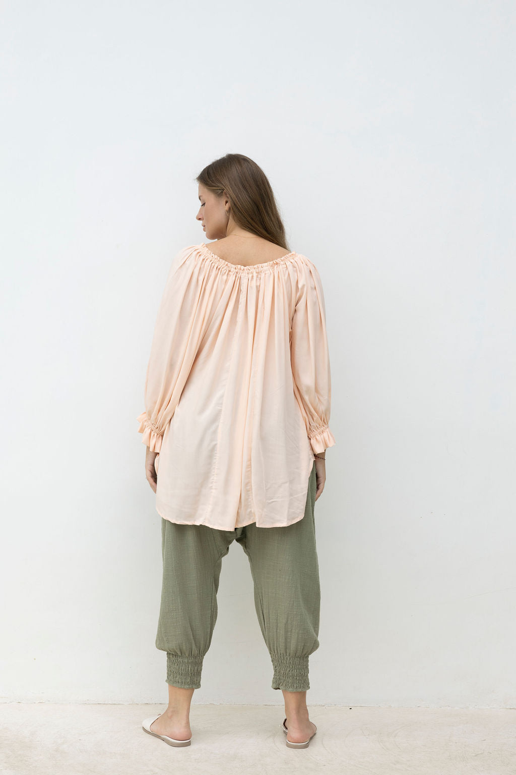 Woman wearing a light pink blouse and green pants against a white background