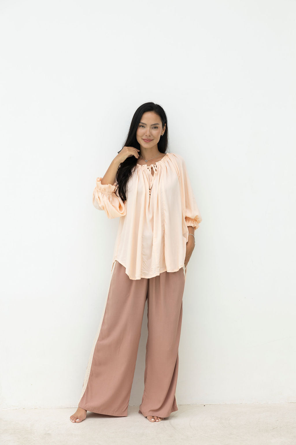 Woman wearing a peach blouse and brown pants on a white background
