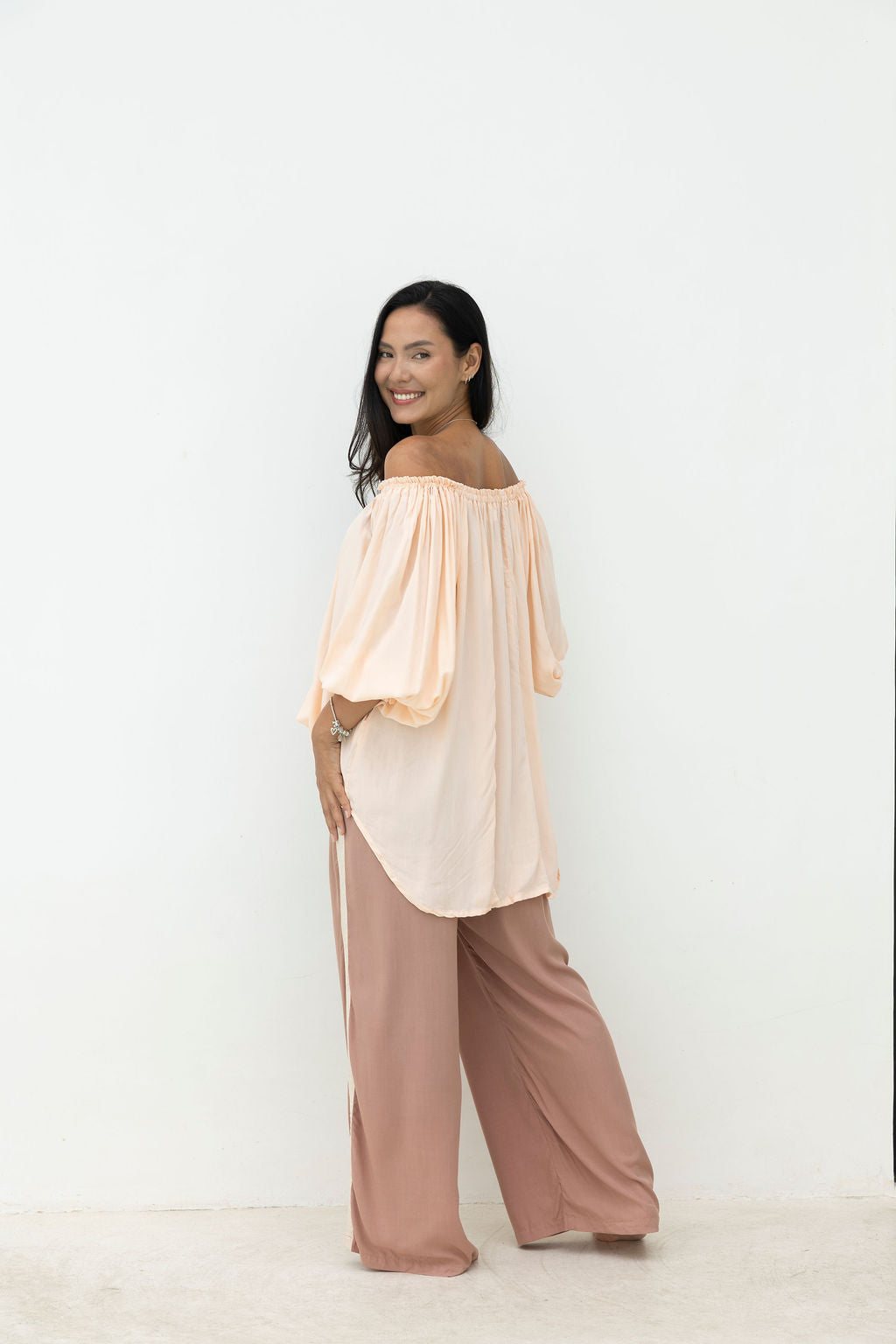 Woman wearing a peach off-shoulder top and pink pants on a white background