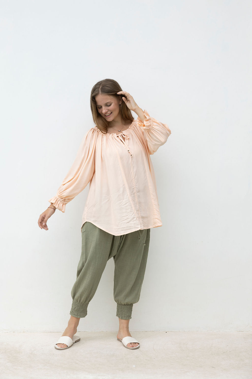 Woman wearing a light pink blouse and green pants against a white background