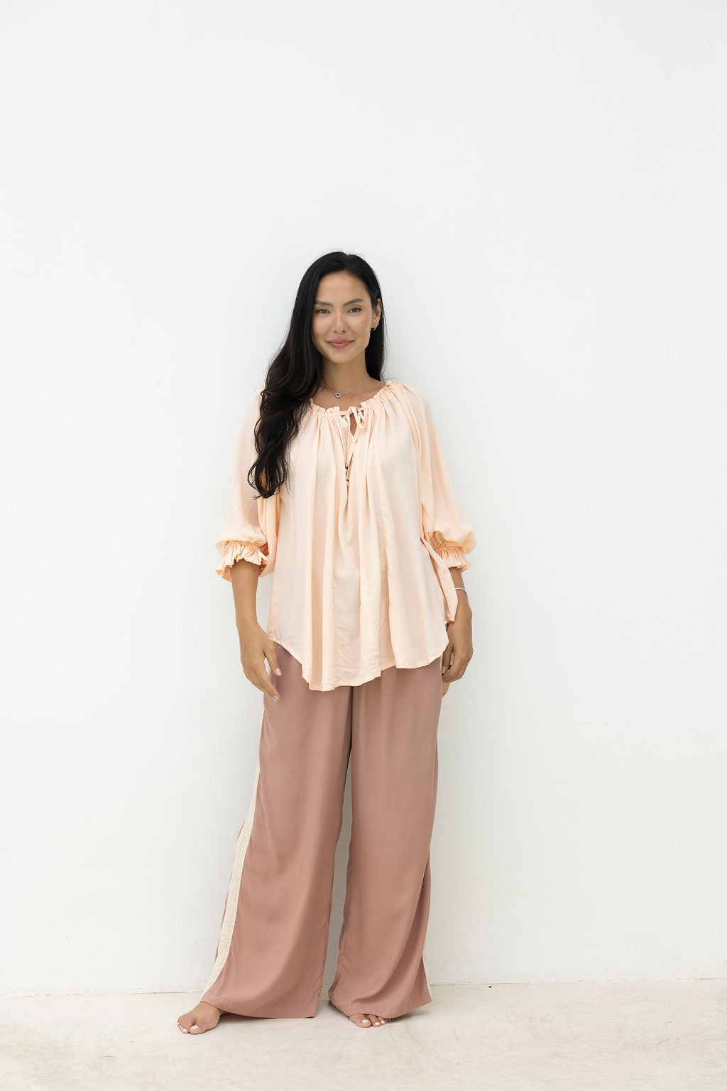 Woman wearing a peach blouse and pink pants on a white background