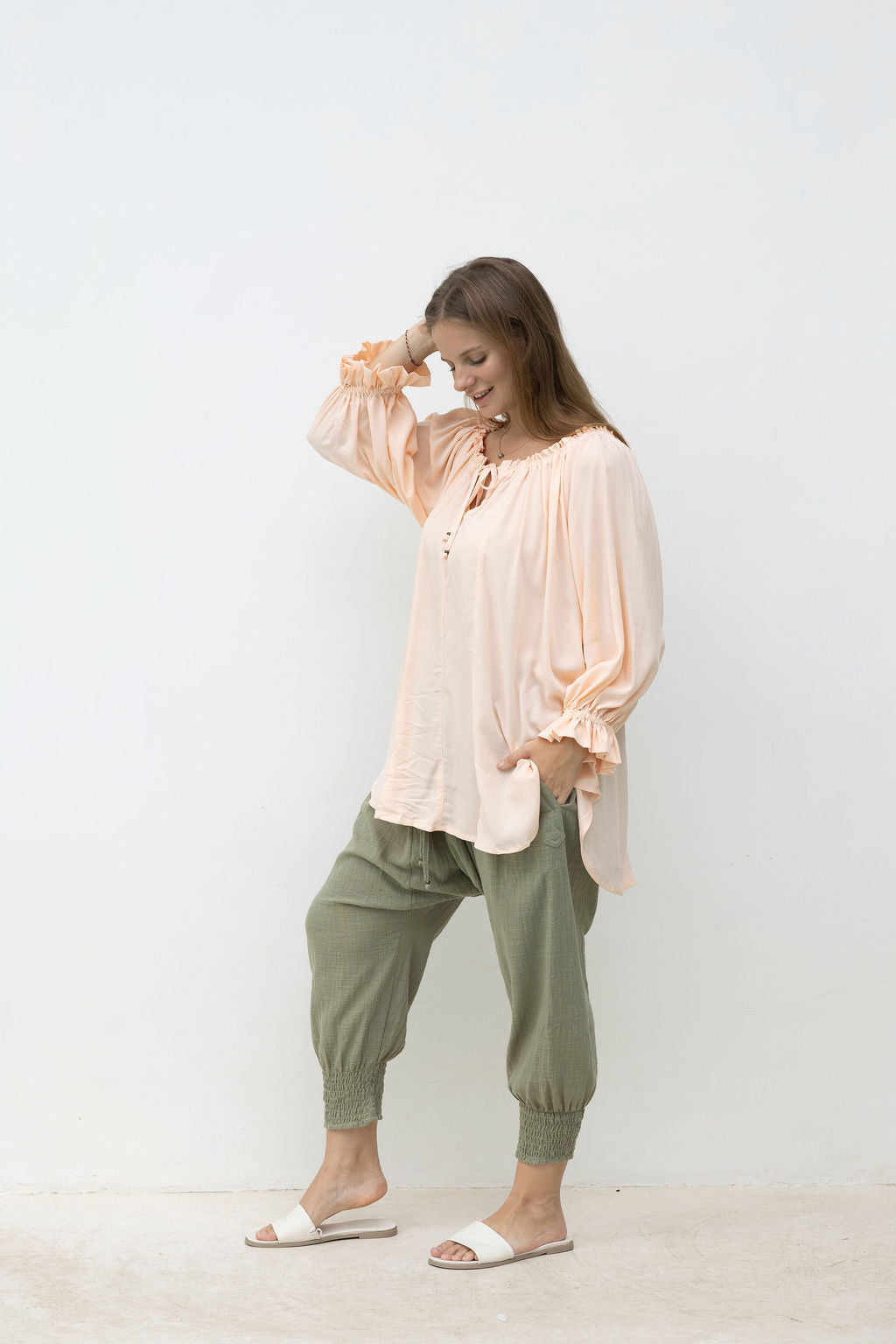 Woman wearing a light pink blouse and green pants against a white background