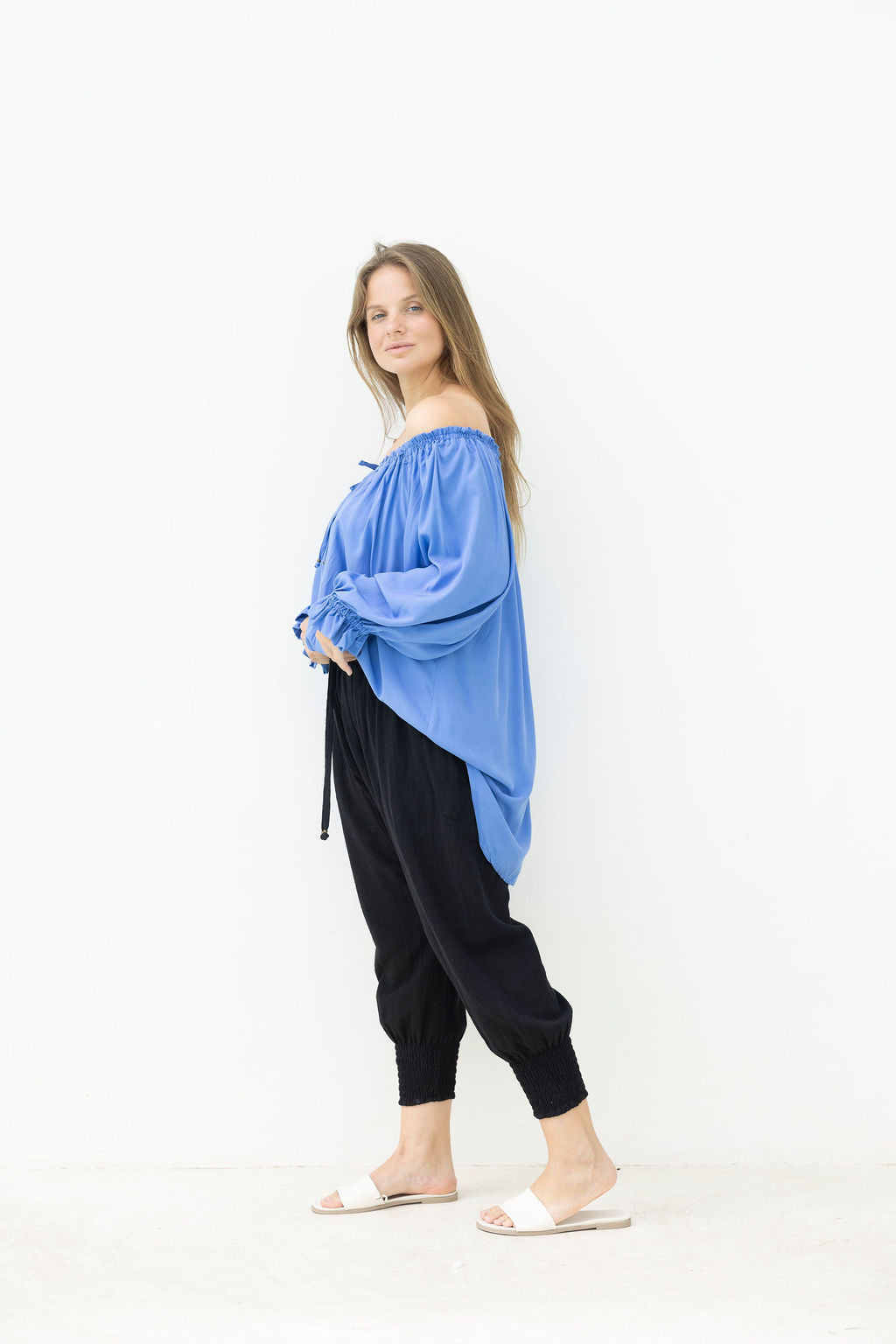 Woman wearing a blue off-shoulder top and black pants on a white background