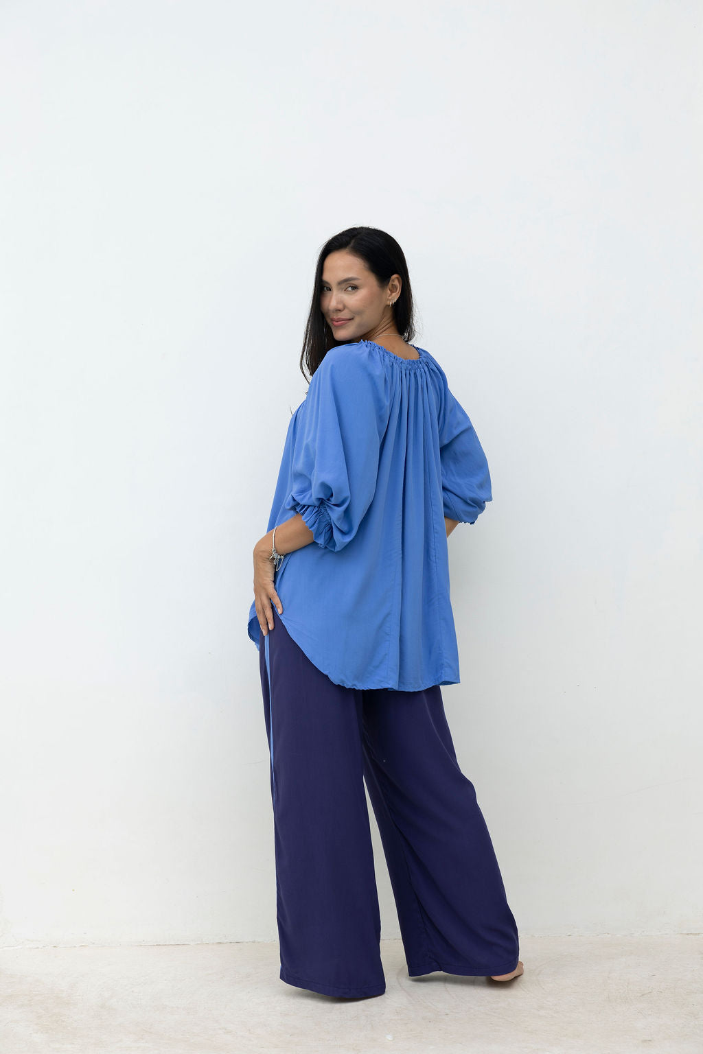 Woman wearing a blue top and dark blue pants against a white background