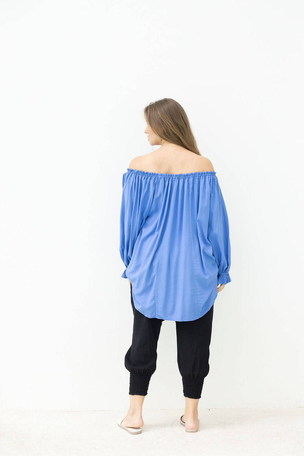 Woman wearing a blue off-shoulder top and black pants on a white background