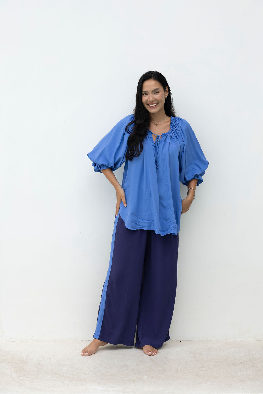 Woman wearing a blue top and wide-leg pants against a white background