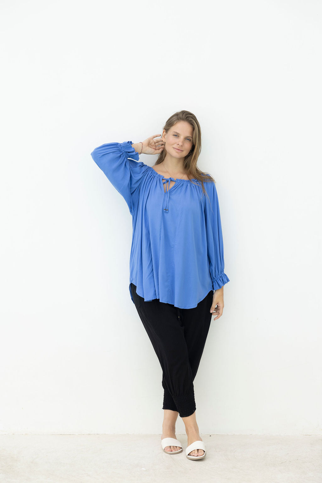 Woman wearing a blue top and black pants against a white background