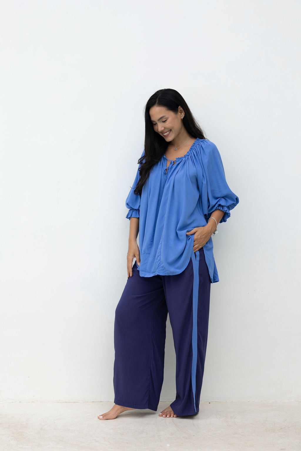 Woman wearing a blue top and dark blue pants against a white background