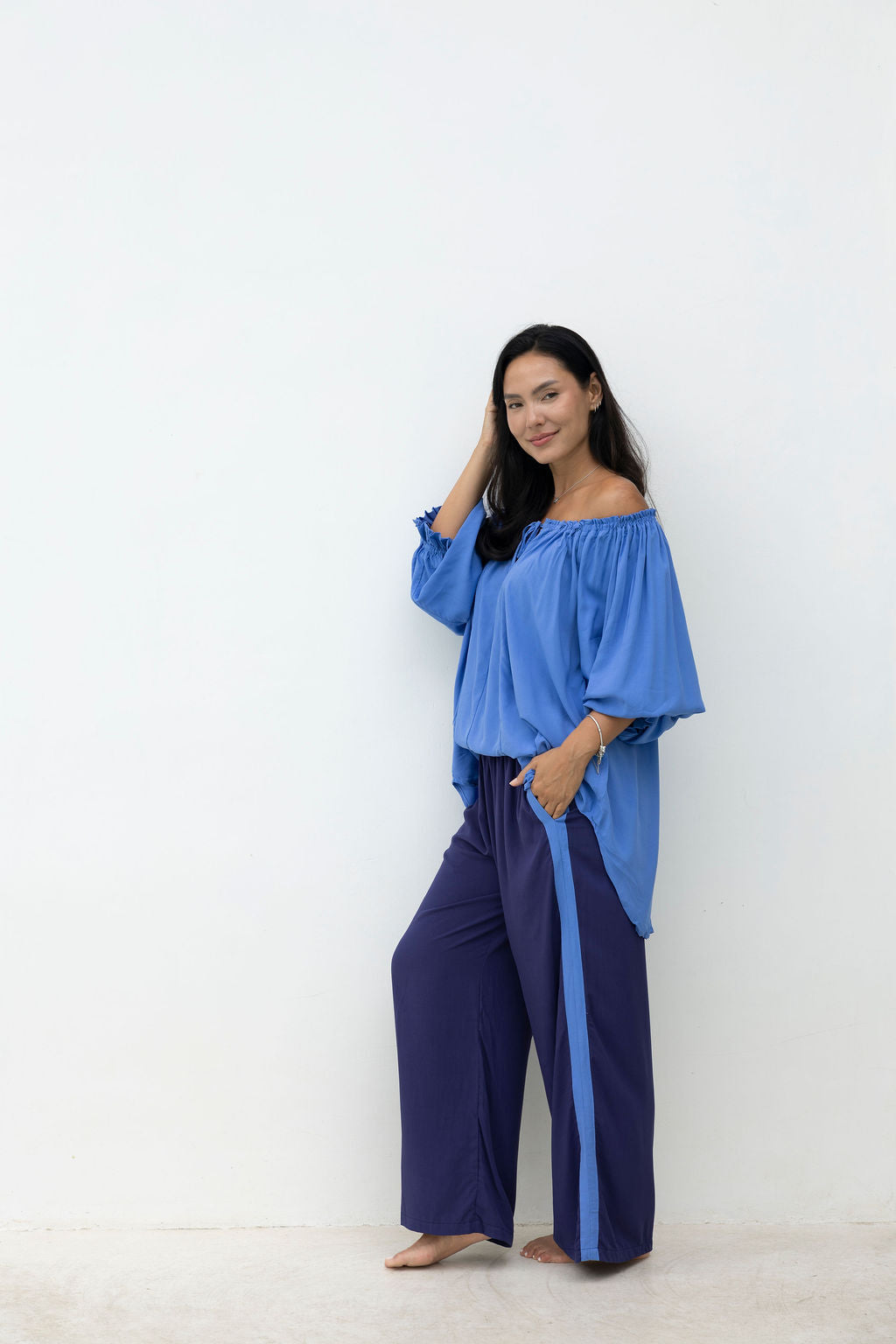 Woman wearing a blue off-shoulder top and navy pants against a white background