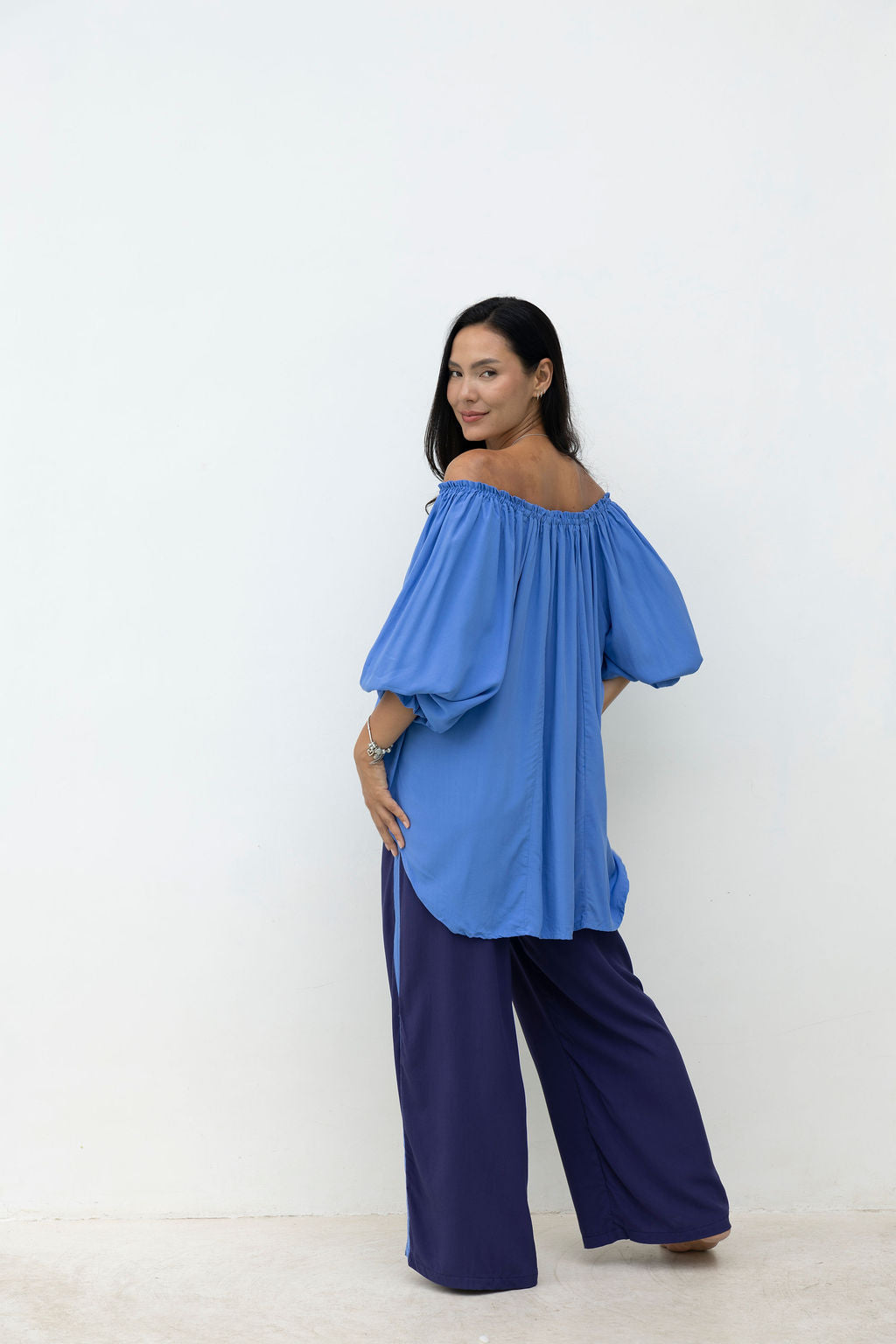 Woman wearing a blue off-shoulder top and navy pants on a white background