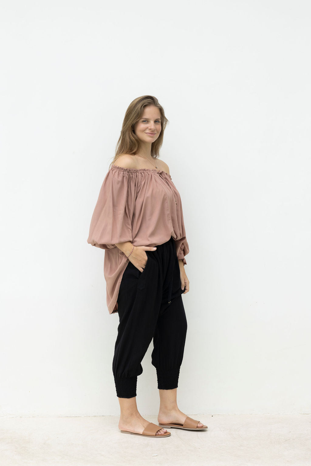 Woman wearing a pink off-shoulder top and black pants on a white background