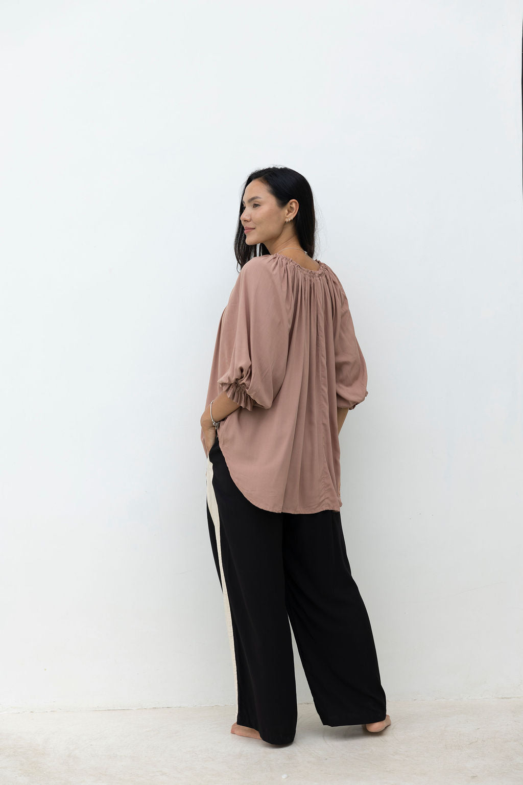 Woman wearing a brown blouse and black pants against a white background