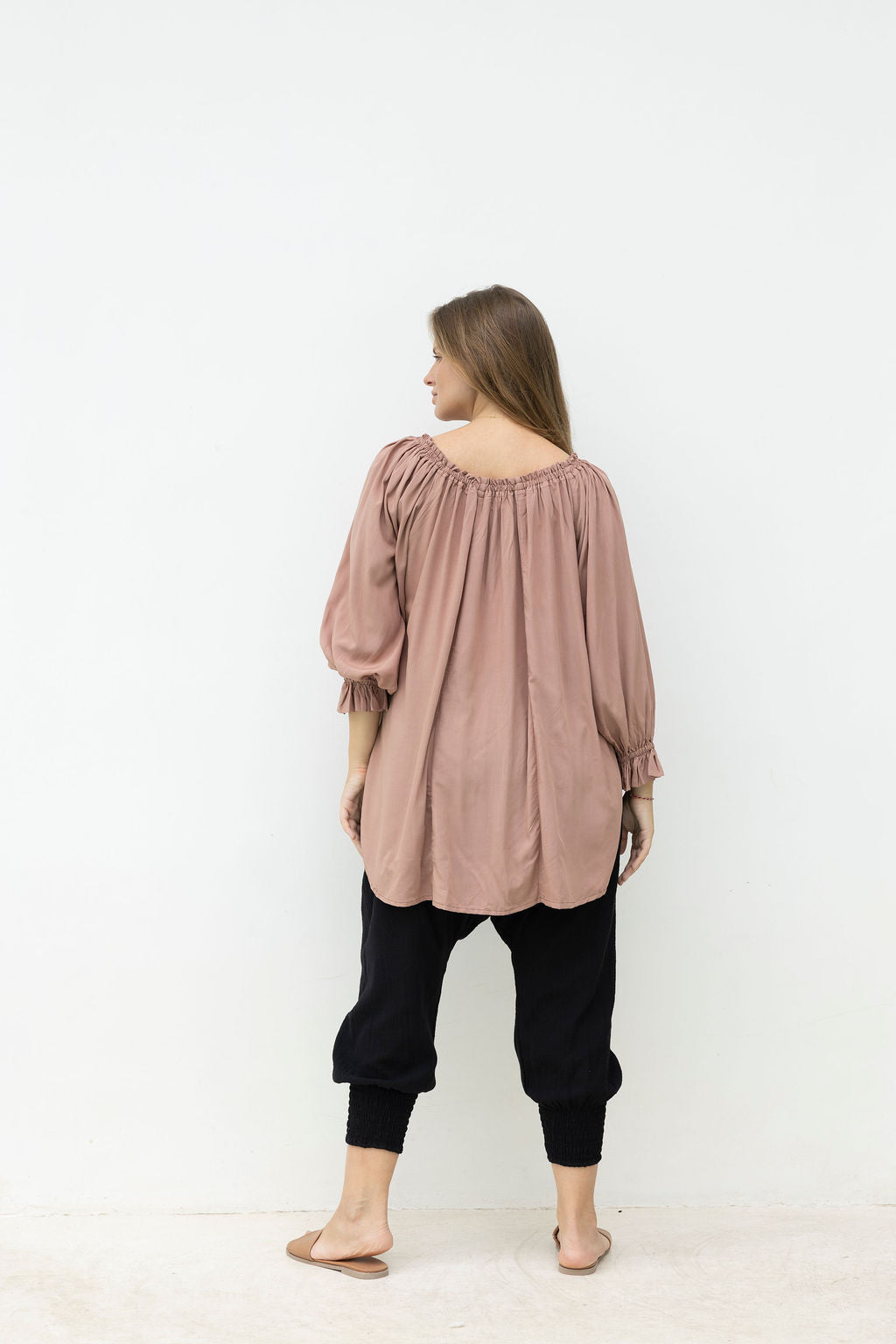 Woman wearing a long, light brown blouse and black pants on a white background