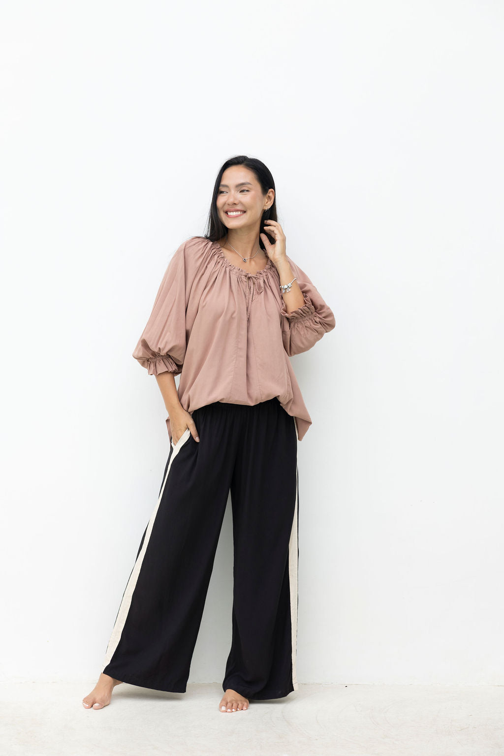 Woman wearing a pink blouse and black pants against a white background