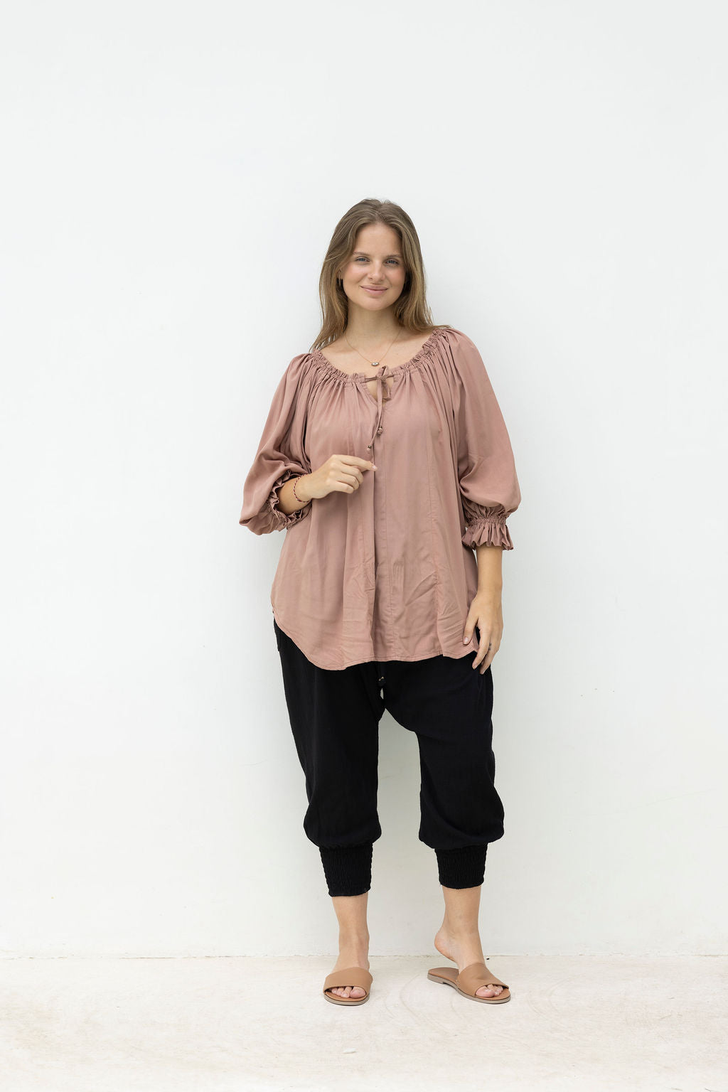 Woman wearing a pink blouse and black pants on a white background