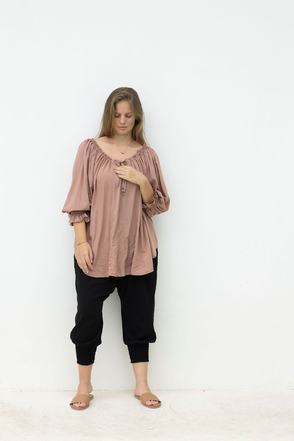 Woman wearing a pink blouse and black pants against a white background