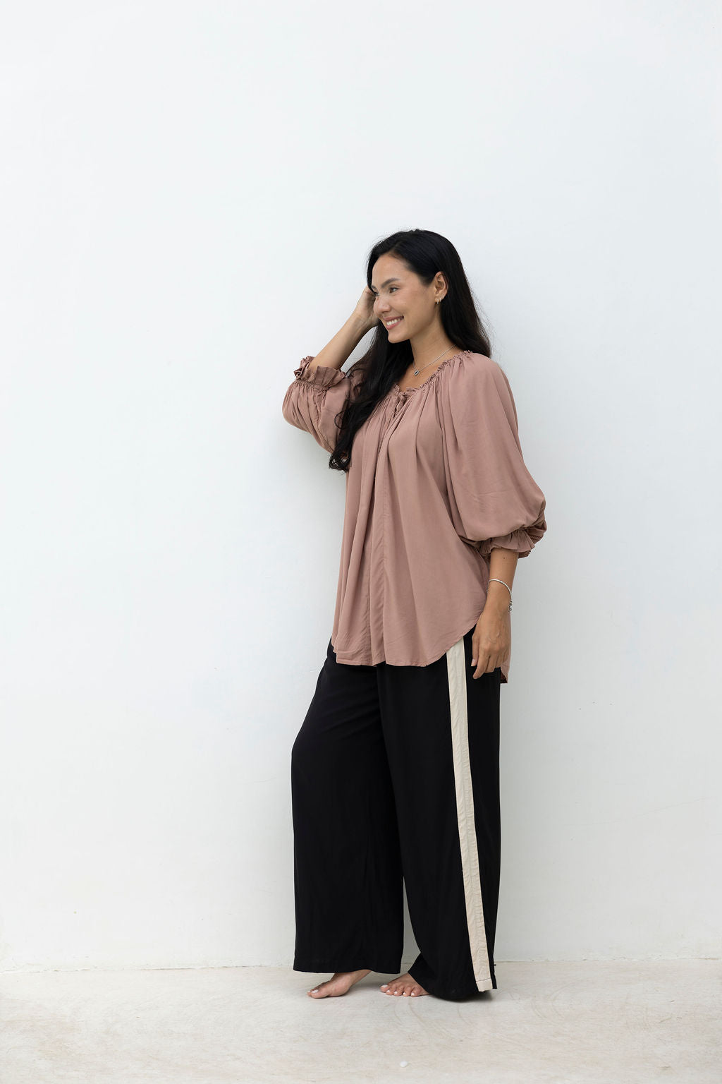 Woman wearing a pink blouse and black pants against a white background