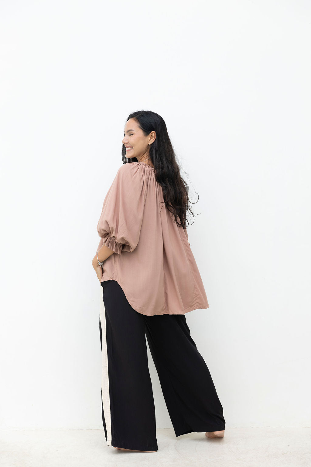Woman wearing a pink blouse and black pants on a white background