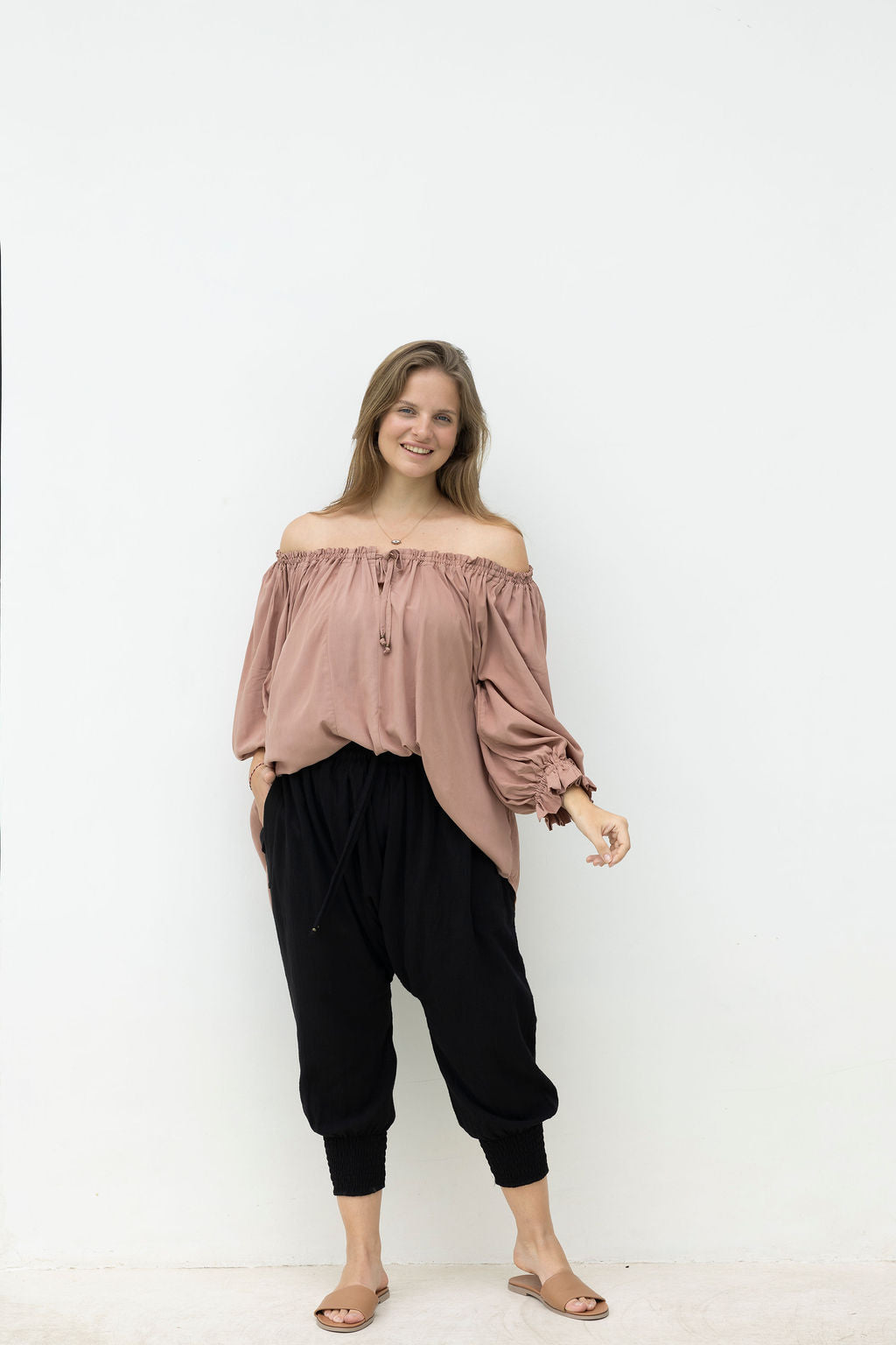 Woman wearing a pink off-shoulder top and black pants on a white background