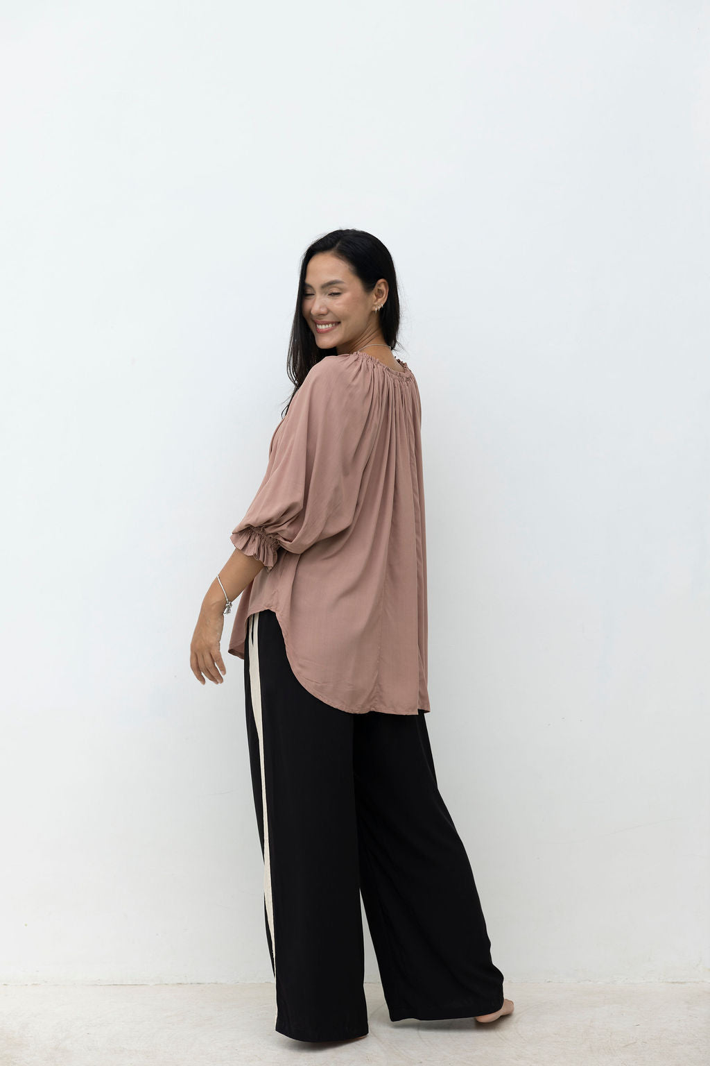 Woman wearing a loose-fitting, long-sleeve top and wide-leg pants on a white background