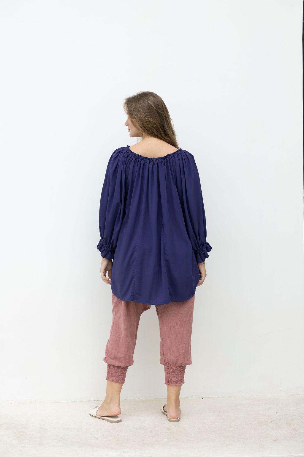 Woman wearing a blue top and pink pants against a white background