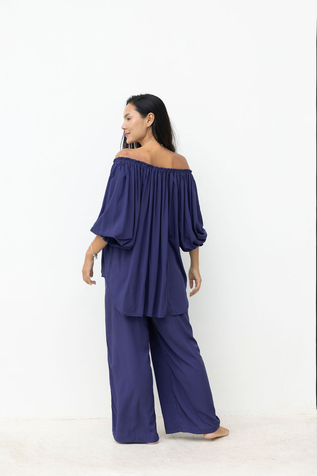 Woman wearing a purple off-shoulder top and wide-leg pants on a white background
