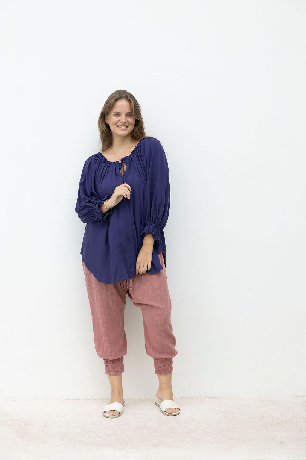 Woman wearing a blue top and pink pants against a white background