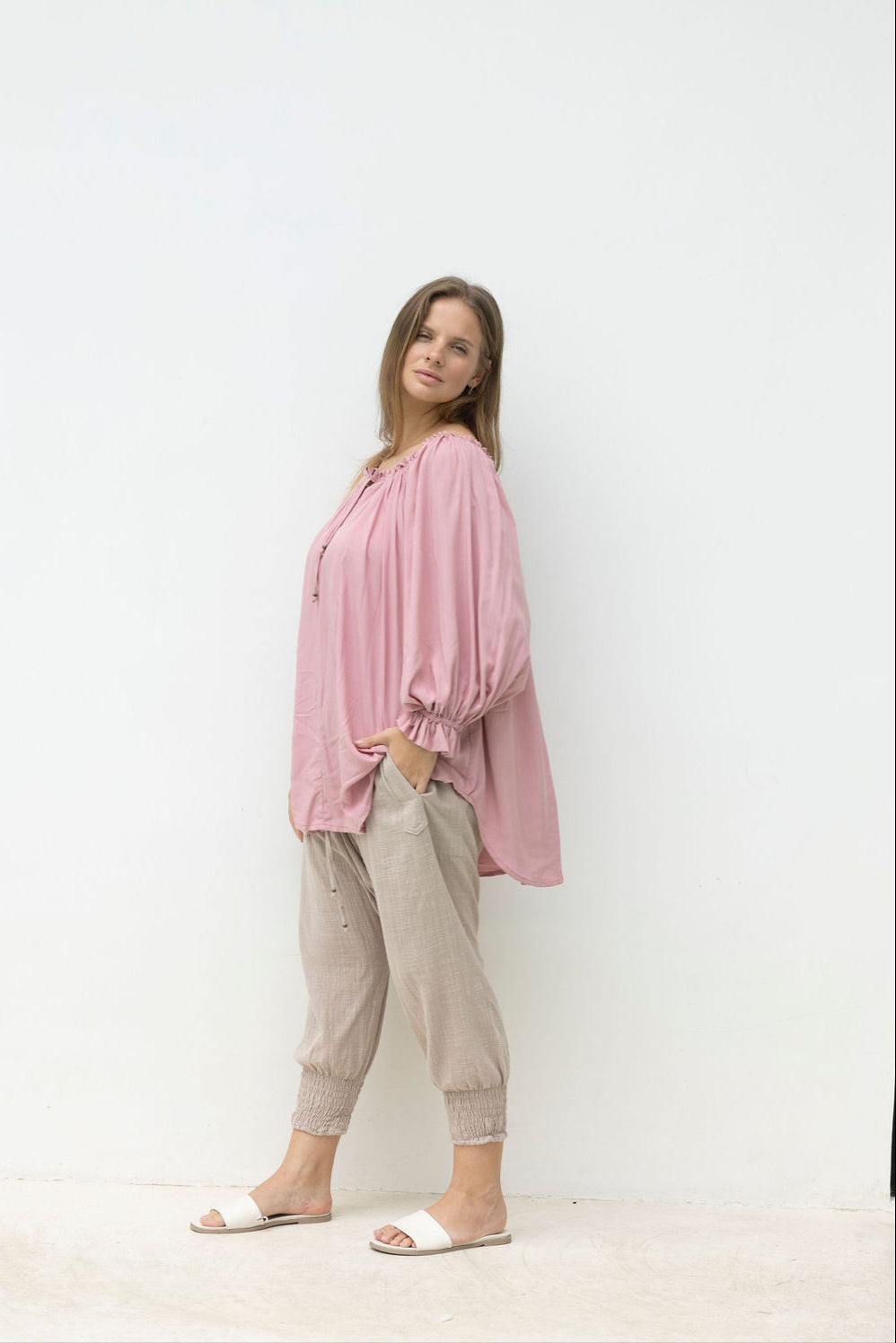 Woman wearing a pink blouse and beige pants against a white background