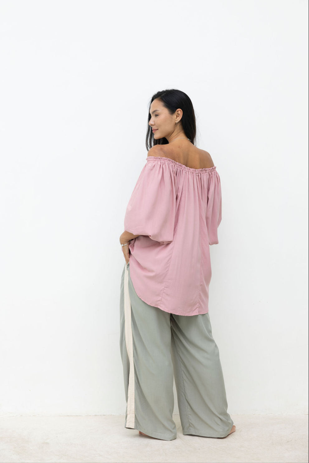 Woman wearing a pink off-shoulder top and light gray pants on a white background