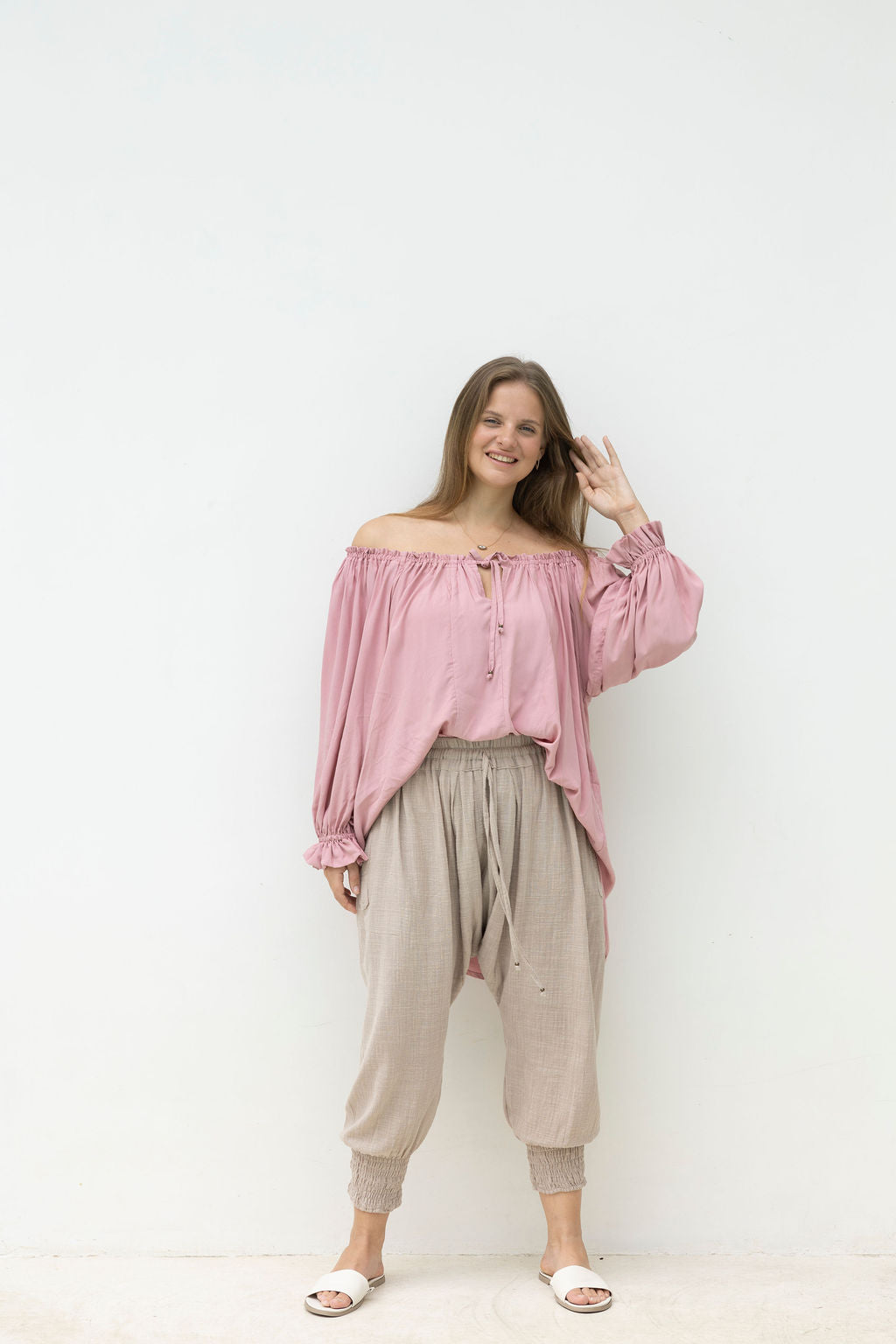 Woman wearing a pink off-shoulder top and beige pants against a white background